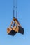 Clamshell bucket suspended by wire ropes and chains against the blue sky