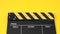 Clapperboard or movie slate with black&yellow color and film roll on yellow background. It is used in video production and film