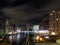 Clarence dock leeds at night with moored barges and moonlit clouds over brightly illuminated waterside buildings reflected in the