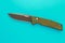 Clasp-knife on a turquoise background. Pocketknife of military color. Single object. Metallic jackknife.