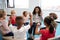 A class of infant school children sitting on chairs in a circle in the classroom, raising hands and learning to count with their f