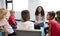 A class of infant school children sitting on chairs in a circle in the classroom talking to their female teacher