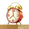 Classic alarm clock with red body and golden bells, on a table.