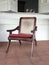 Classic antique wooden chair with mesh backrest and red cushion. Front view of colonial solid wood armchair on porch of tropical