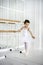 Classic ballet dancer child posing at barre on rehearsal room background. 6 years old girl in white ballet clothes with mirrors on