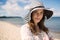Classic beautiful woman in hat standing on beach smirking