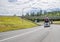 Classic big rig car hauler white semi truck transporting cars on the hydraulic semi trailer driving on the turning highway road