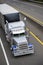 Classic big rig gray semi truck with powerful grille guard and covered semi trailer running on the multiline highway road