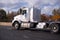 Classic big rig semi truck with storage unit and flat bed trailer going on the autumn road