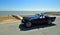 Classic Blue Daimler Dart SP250 being driven along seafront promenade.