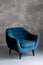 Classic blue velvet art deco armchair with wooden legs against a gray wall. Front view. Soft selective focus