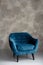 Classic blue velvet art deco armchair with wooden legs against a gray wall. Front view. Soft selective focus