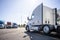 Classic bonnet big rig white semi truck tractor stand on the truck stop parking lot across another semi trucks standing in row for