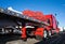 Classic bright red American big rig semi truck with flat bed semi trailer standing on the truck stop with covered cargo