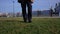 Classic brown shoes in blue pants walk across the green grass with flowers in the city park close-up.