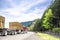 Classic burgundy big rig semi truck transporting stocked plywood on two flat bed semi trailers running on the winding mountain