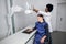 Classic ceiling-mounted x-ray system. Young African woman doctor radiologist and male Caucasian patient in x-ray room