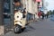 A classic, elegant Vespa scooter parked on a pedestrian sidewalk in the city center street