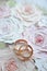 Classic golden wedding rings on the floral painted roses background. Invitation card