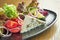 A classic, healthy Greek salad with homemade feta cheese, red onion, tomatoes and lettuce on a black plate on a wooden background