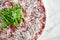 Classic Italian appetizer - veal carpaccio with arugula and parmesan served on a white plate on a marble background. Thinly sliced