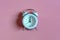 Classic mechanical alarm clock showing 12 o`clock on a pink background