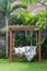 Classic outdoor wooden swing in the green garden with pillows and blanket.