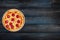 Classic pepperoni pizzai on a wooden stand on a dark wooden background. Top view orientation on the left side