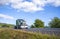 Classic powerful green big rig bonnet semi truck tractor running on summer road with cloud sky