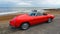 Classic red Alfa Romeo Sports  Convertible Car parked on seafront promenade.