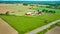 Classic red barn farmyard with green pastures and farmland aerial with distant dirt fields