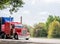 Classic red big rig semi truck with framed covered semi trailer driving on the road to point of delivery