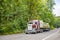 Classic red big rig semi truck tractor carry lumber wood on flat bed semi trailer running on the winding road in green forest