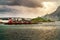 Classic red cabins in a line in Lofoten, Norway. Faded rainbow background with flying birds and a setting sun. Foreground set with