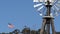 Classic retro windmill, bladed rotor and USA flag against blue sky. Vintage water pump wind turbine, power generator on livestock