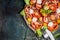 Classic salad with tomatoes and mozzarella in aged metal plate with cutlery on dark rustic background, top view, place for text