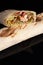 Classic shawarma kebab pita with chicken and vegetables and sauce on a black background. in section