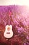 Classic small guitar laid on a lavender field row under the sunrise rays