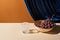 Classic still life with grape, glass on beige table near velour curtain isolated on orange