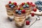 Classic tiramisu dessert with blueberries and raspberries in a glass and bowls with berries on concrete background