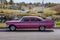 Classic vintage retro american pink car of 1959 from side proection, settled in front of a village landscape.