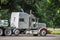 Classic white big rig semi truck tractor with loaded flat bed semi trailer standing on the rest area parking lot parallel to the