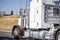 Classic white and brown big rig semi truck tractor with protection wall on the cab back driving on the road