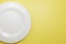 Classic white ceramic plate for a restaurant or cafe view from the top on a yellow Pastel background. An excellent blank for an
