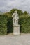 Classic white marble statue of woman with flute in green garden park. Ancient Roman or Greek woman stands on podium. the statue is