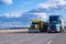 Classic yellow and blue modern semi trucks side by side on the r