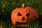 Classical carved gouged out pumpkin Hallowen Jack O Lantern lying with triangular eyes and nose on green lawn with autumn leaves,