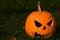 Classical carved gouged out pumpkin Hallowen Jack O Lantern lying with triangular eyes and nose on green lawn with autumn leaves,