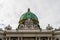 Classical, typical Viennese architecture in the middle of the old city centre, with white clouds and blue sky above. A green dome