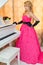 Classy blonde in long red dress is standing next to the piano